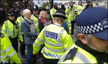 Two Socialist Party members standing their ground surrounded by police, photo Sarah Wrack