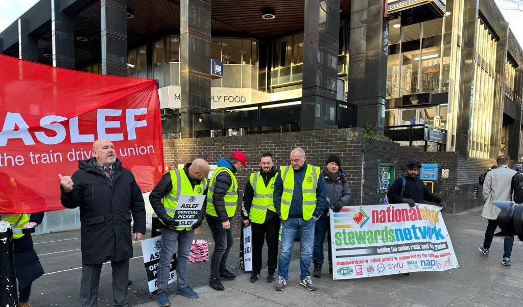 Euston Aslef picket line, with Rob Williams (NSSN and Socialist Party, in grey coat) holding NSSN banner. 1.2.23