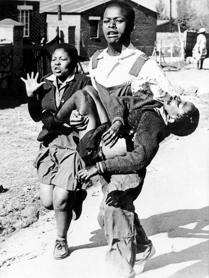 Hector Pieterson carried by Mbuyisa Makhubo after being shot by the South African Police. Hist sister, Antoinette Sithole, runs beside them. Pieterson was rushed to a loacl clinic, where he was declared dead on arrival. This photo by Sam Nzima became an icon of the Soweto uprising Photo: Public Domain